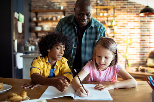Older man helping kids with homework at kitchen table