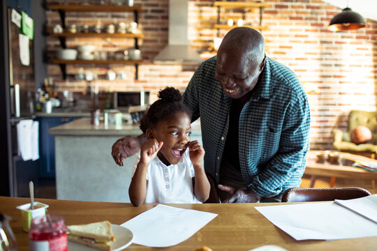 Grandfather cheering with granddaughter at kitchen table