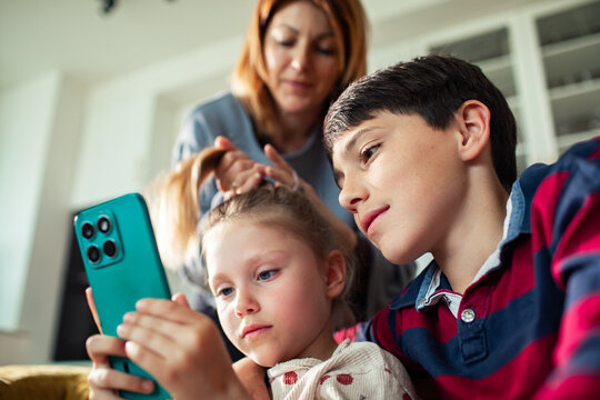 Boy and girl watch smartphone as parent does hair