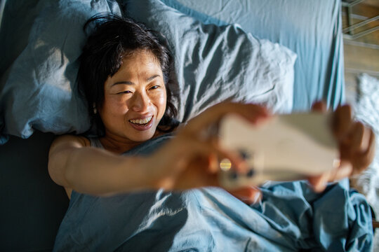 Smiling woman taking a selfie in bed