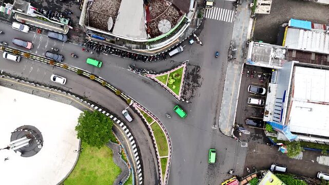 Aerial view of traffic moving around a triangular roundabout with green landscaping in the city center of Sukabumi, West Java, Indonesia.