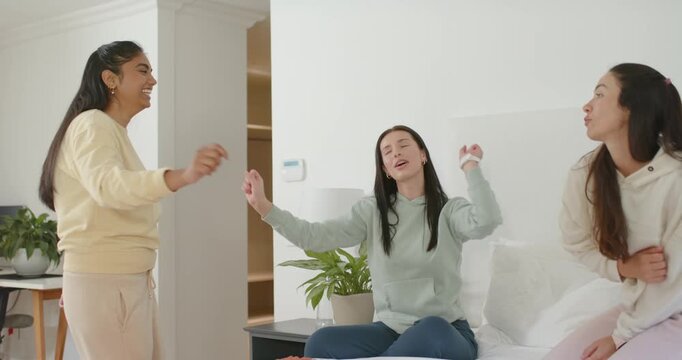 Three female friends in loungewear sharing joke, breaking into in-sync dancing and miming on bed