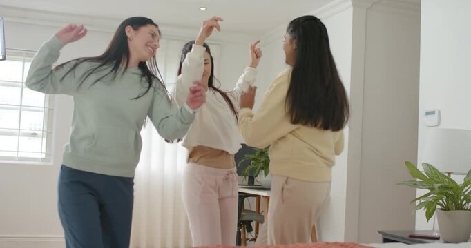 Diverse female friends gathering at foot of bed in sweats for bonding, dancing and mirroring moves
