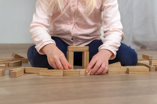 Child sitting on a wooden floor, intently engaging in constructive play, using natural wooden blocks to build a small structure, highlighting focus and developing motor skills and creativity