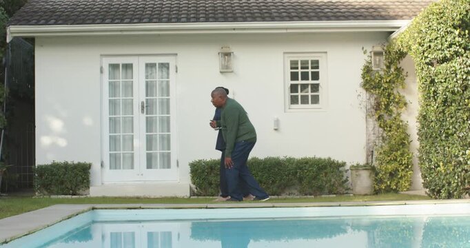 Couple walking along pool edge by house, woman checking smartphone toward gate, copy space