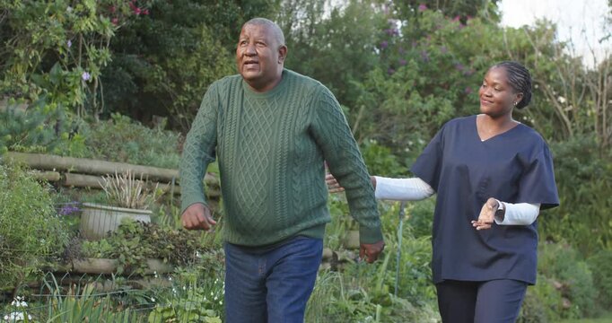 African American caregiver in scrubs initiating walk, offering hand while senior man walking path