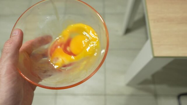 Hand holding a glass bowl with raw cracked eggs, representing home cooking, meal preparation, breakfast ingredients and everyday food preparation