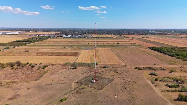 Aerial view of the Lakihegy radio mast above harvested fields and rural outskirts of Szigetszentmikl&oacute;s, Hungary, under a blue late-summer sky.