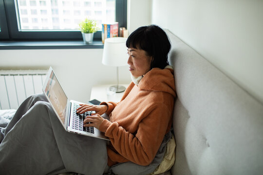Woman working on laptop in bed at home