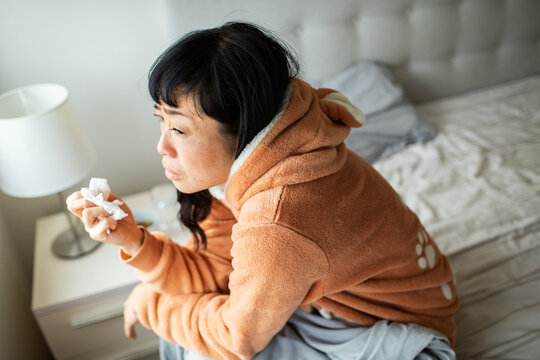 Sick woman holding tissue on bed at home