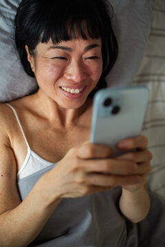 Smiling woman using smartphone in bed at home
