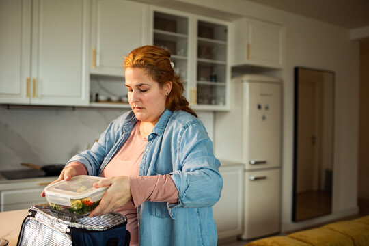Woman packing salad into insulated lunch bag at home