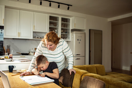 Woman helping boy with homework at kitchen table