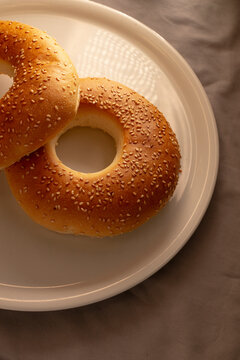 Golden sesame crust bagels rest on white round ceramic plate, photographed from overhead with soft neutral background emphasizing toasted texture and sesame seeds.