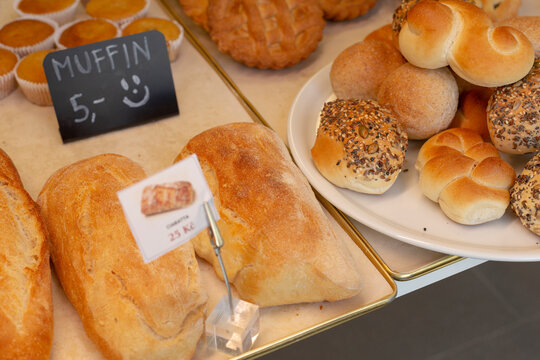 Close-up of assorted freshly baked breads, seeded rolls, and loaf slices on metal trays and white plate in bakery display case.