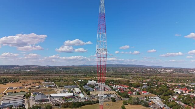 Aerial view of the Lakihegy radio mast above industrial buildings, homes and dry fields in Szigetszentmikl&oacute;s, Hungary, beneath a blue sky with scattered clouds.
