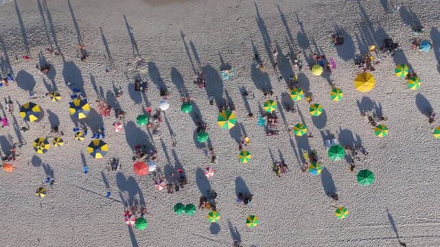 Top-down aerial view of beachgoers and colorful umbrellas dotting the sand on Copacabana Beach, Rio de Janeiro, Brazil.