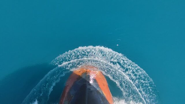 Aerial top-down shot of a ship bow cutting through clear turquoise ocean waves, tilting up to reveal a vast blue horizon.