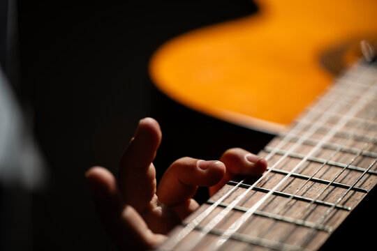Fingers pressing acoustic guitar strings playing music