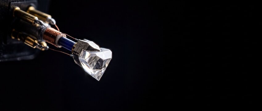 Diamond stylus tip with intricate metal wiring and gold connectors against black background.