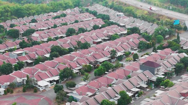 Aerial view of a residential housing complex with uniform houses featuring red roofs, a central roundabout, and lush trees in Indonesia.
