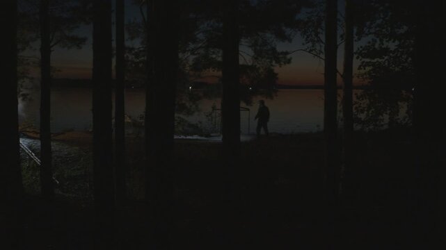 Group of people camping on the river's coast at night. People camping on a river as seen from the forest