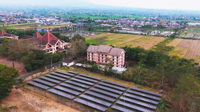 Aerial view of solar panels and buildings surrounded by lush greenery and agricultural fields in Malang, East Java, Indonesia.