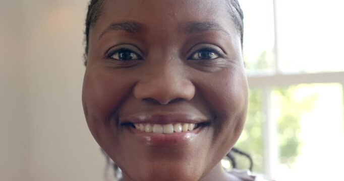 Mid-adult African woman responding to camera prompt, widening smile and laughing in room by window