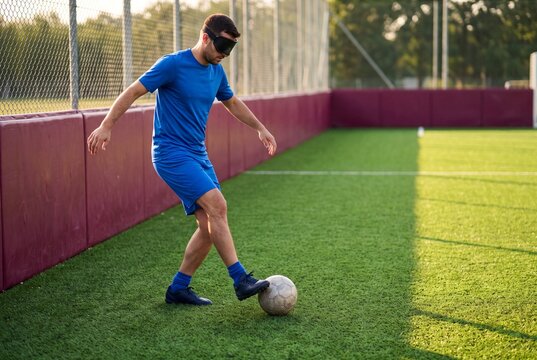 Blindfolded man playing football on green field