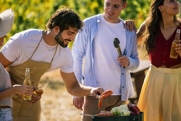 Naklejka premium Man grilling food while friends gather around in a vineyard