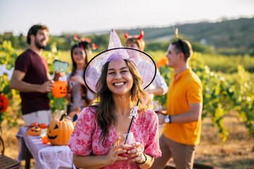 Naklejka premium Smiling woman in witch costume holding a drink at an outdoor Halloween party