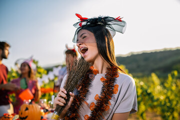 Naklejka premium Woman laughing in a Halloween costume with a decorated broom at a vineyard party
