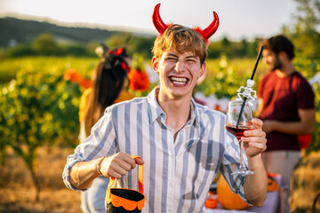 Naklejka premium Smiling man wearing devil horns and holding a wine glass at Halloween