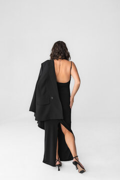 Rear view of elegant forty year old woman in black backless dress with jacket on shoulder.