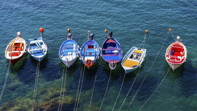 Colourful fishing boats attached to the rock lie in the turquoise water in the harbour of Riomaggiore, Riomaggiore, Ligurian Coast, Liguria, Italy