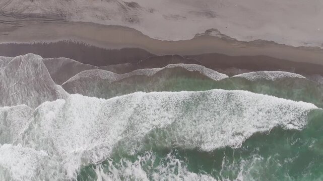 Aerial view of Parangtritis Beach with turquoise waves crashing onto the dark sand coastline in Kecamatan Kretek, Daerah Istimewa Yogya, Indonesia.