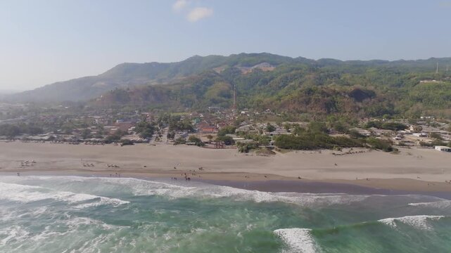 Aerial view of Parangtritis Beach with crashing waves, sandy shore, and coastal village in Kecamatan Kretek, Daerah Istimewa Yogya, Indonesia.