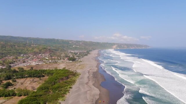 Aerial view of Parangtritis Beach with dark sand, rolling waves, and coastal vegetation in Kecamatan Kretek, Daerah Istimewa Yogya, Indonesia.