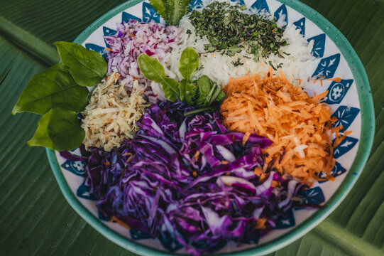 View of a colorful salad bowl with shredded purple cabbage, carrots, red onions, and fresh herbs in a patterned dish on a banana leaf, Puerto Viejo de Talamanca, Limon Province, Costa Rica.