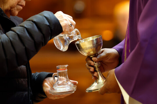 Altar server pours water into chalice as priest holds it during offertory preparation. Thones. France.