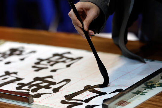 Close-up of a hand holding a calligraphy brush writing bold Chinese characters on gridded paper. Hanoi. Vietnam.