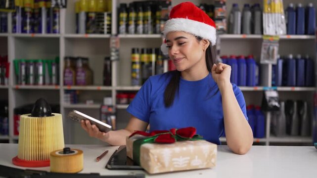 Young latina female mechanic in a santa hat singing while working at an auto parts store during christmas