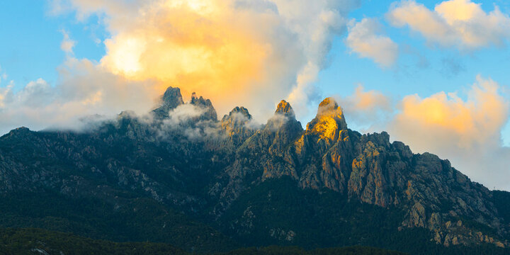 Panoramic aerial view of Aiguilles de Bavella rock formations illuminated at sunset among clouds, Col de Bavella, Zonza, Corsica, France
