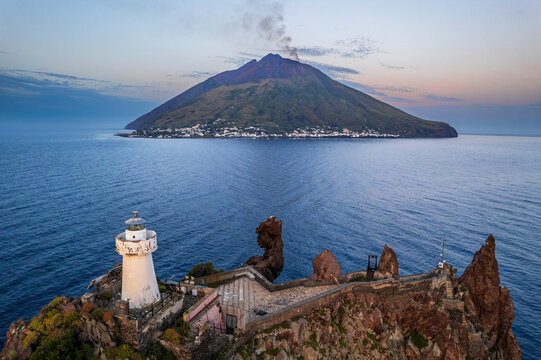 The lighthouse of Strombolicchio and the volcano Stromboli with smoke in the backgroun at dusk, Messina province, Tyrrhenian Sea, Mediterranean Sea, Sicily, South of Italy,, Italy