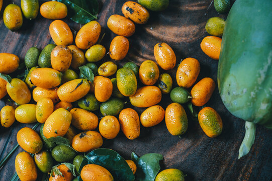 View of a collection of fresh orange kumquats and a large green papaya on a dark wooden surface, Puerto Viejo de Talamanca, Limon Province, Costa Rica.