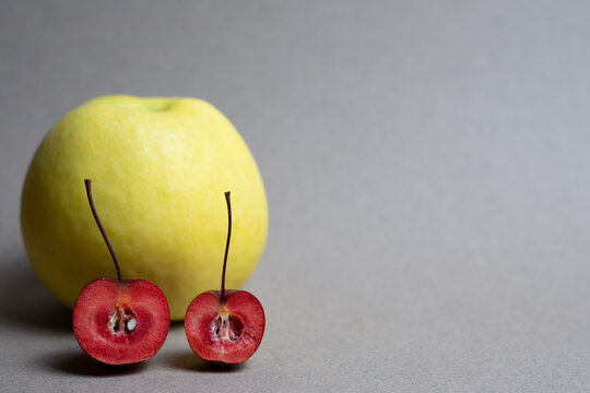 Small Red Crab Apples and Large Yellow Apple on Neutral Background with Copy Space
