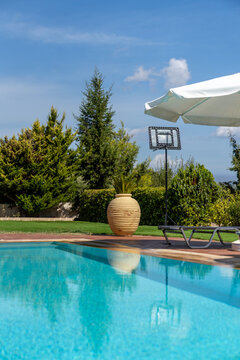 Swimming pool with turquoise water, sun lounger, and terracotta pot in a lush resort garden on a sunny day
