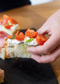 Hand holding focaccia with stracciatella cheese, cherry tomatoes and basil, Italian appetizer