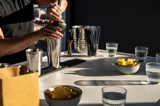 Bartender muddling a cocktail in a stainless shaker at a rooftop bar