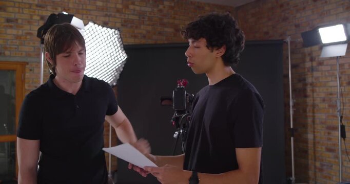 Diverse male colleagues in studio wearing black tees, placing guiding hand and rehearsing lines